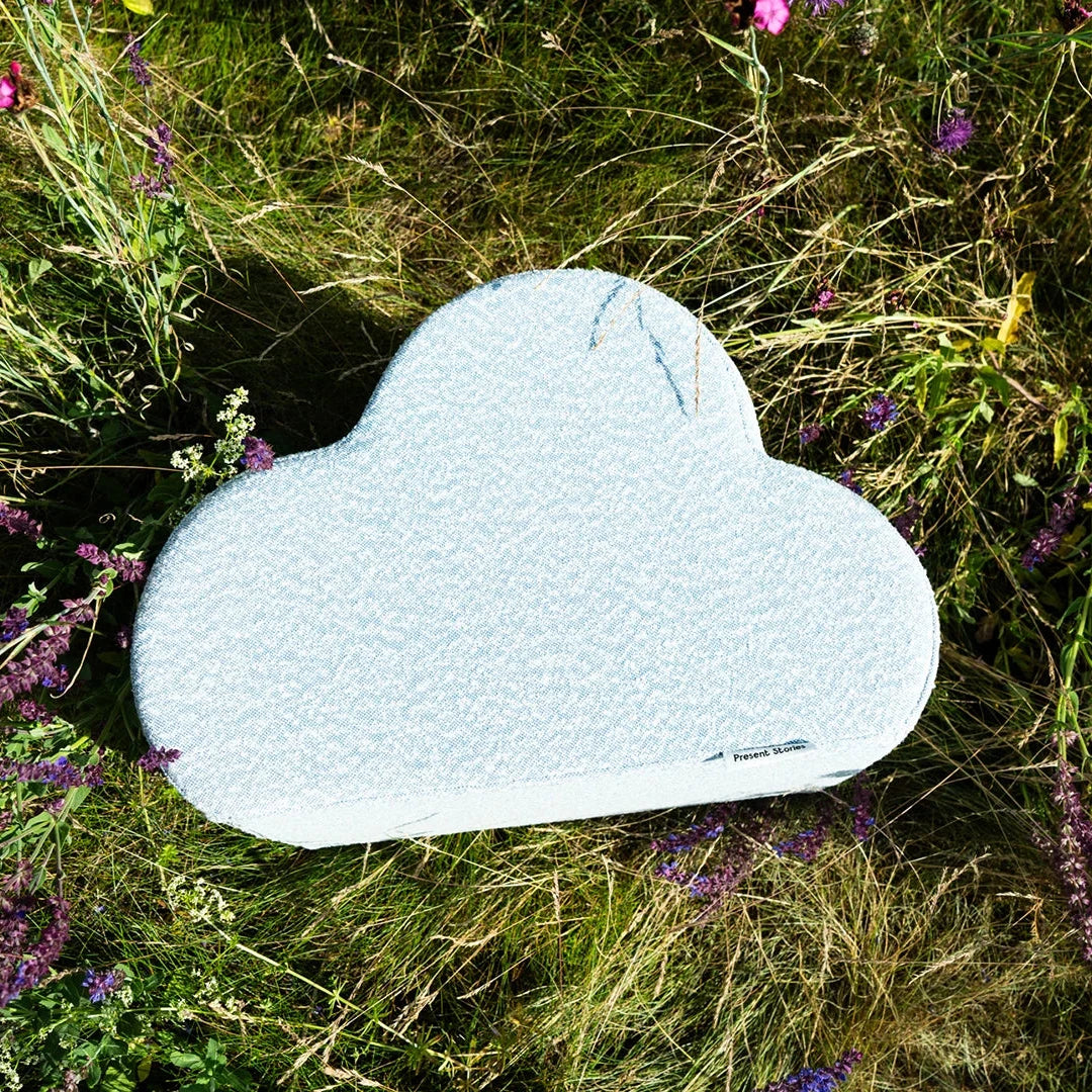 Das Cloud Kissen von Present Stories liegt als stilvolles Designobjekt in einer Sommerwiese zwischen Wildblumen – inspiriert von Natur und Form