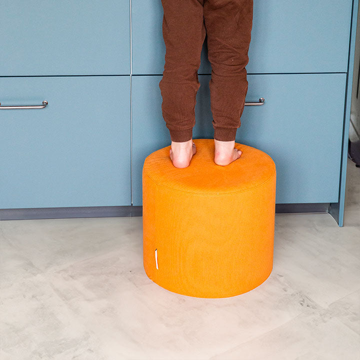 Kind steht auf einem orangen Pouf von Present Stories – robuste Softbausteine als vielseitige Spielmöbel und praktische Helfer im Familienalltag.
