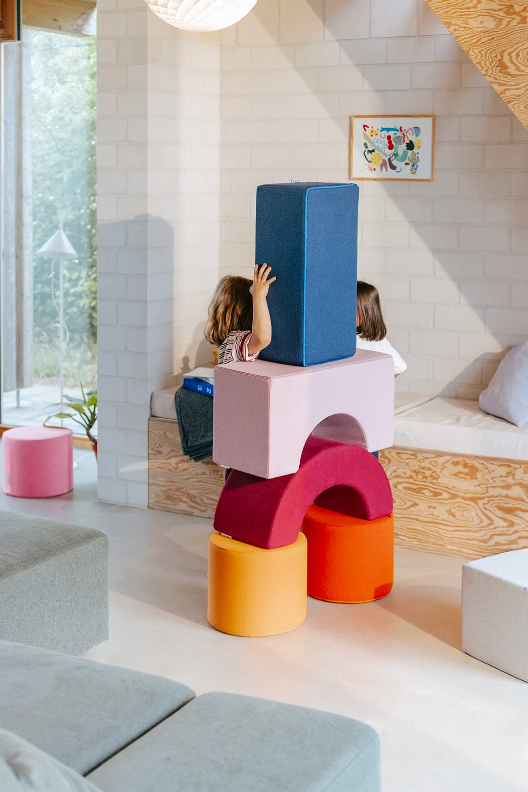 Kinder bauen einen hohen Turm aus Present Stories Softbausteinen – bunte XXL Bausteine in Form von Brücke, Wippe, Zylinder und Pouf aus Schaumstoff für kreatives Bauen, Softplay und motorische Förderung im Kinderzimmer.