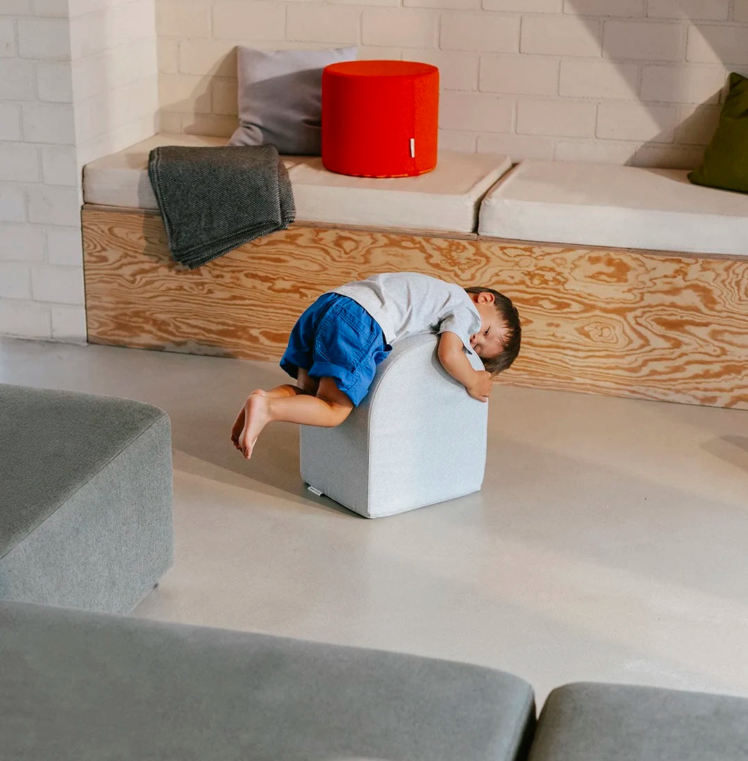 Kind liegt spielerisch auf einem Present Stories Softbaustein  – robuster Schaumstoff Baustein als Teil der XXL Softplay Serie, ideal für Bewegung, Balance und kreatives Spielen im Kinderzimmer.