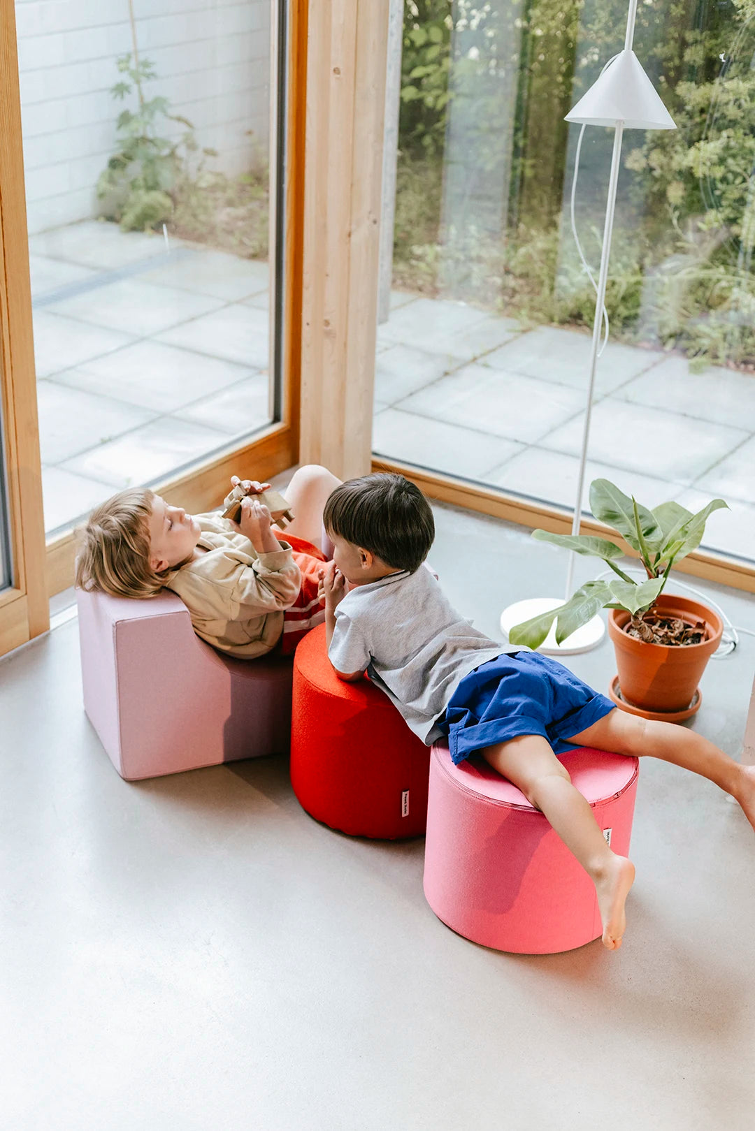 Zwei Kinder spielen und liegen entspannt auf Present Stories Softplay Bausteinen – multifunktionale XXL Schaumstoff Bausteine für fantasievolles Spielen, Sitzen und Entspannen im Kinderzimmer.